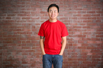 Obraz na płótnie Canvas Asian man in blank red t-shirt standing against brick wall