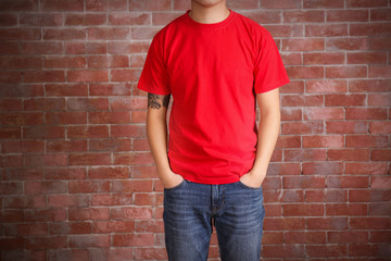 Obraz na płótnie Canvas Young man in blank red t-shirt standing against brick wall, close up