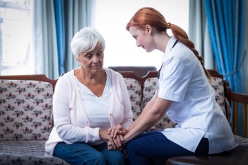 Female doctor consoling senior woman in living room