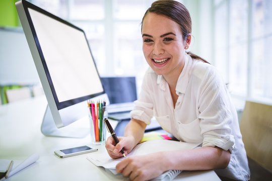 Happy graphic designer writing on book at desk