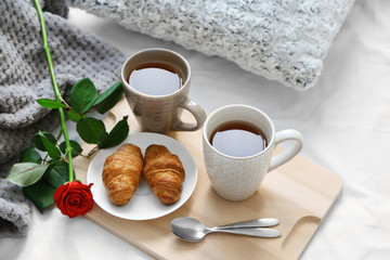 Cups of tea, croissants and rose on wooden tray. Romantic breakfast in bed