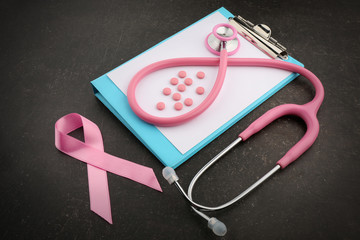 Stethoscope, clipboard, pills and pink ribbon on dark background, breast cancer concept