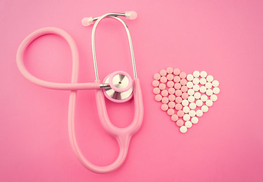 Stethoscope and pills in shape of heart on pink background