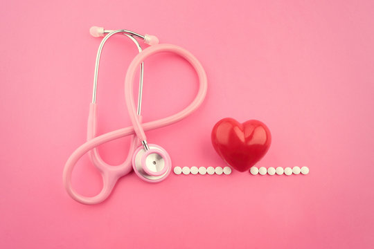 Stethoscope, pills and red heart on pink background