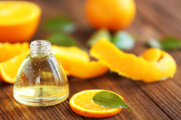 Bottle of essential oil, leaf and slices of orange on wooden table