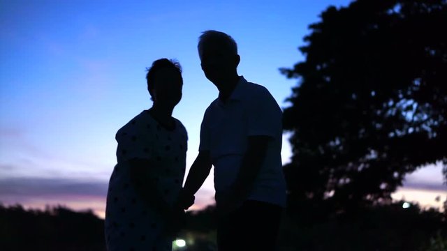 Asian senior silhouette holding hand next to lake. Early morning before sunrise. Beautiful nature