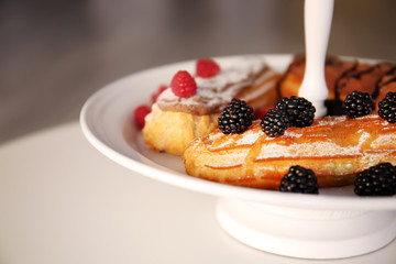 Delicious colourful eclairs with berries and fruit on plate, close up