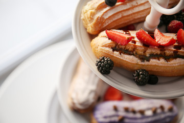 Delicious colourful eclairs with berries on dessert stand, closeup