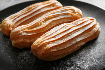 Delicious eclairs with sugar powder on black plate