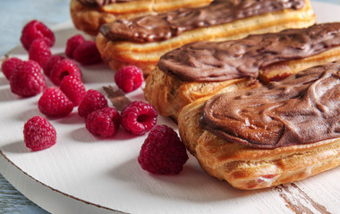 Delicious eclairs with chocolate and raspberry on wooden background