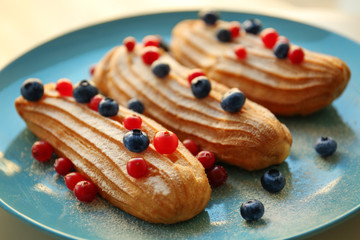 Tasty eclairs with berries on blue plate