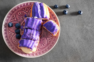 Tasty eclair with berries on pink plate and grey background