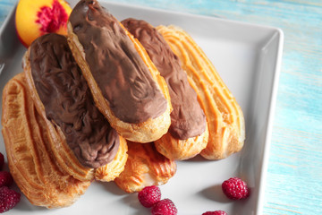 Delicious eclairs with chocolate, peach and raspberry on plate and wooden table