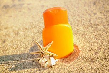 Sunscreen cream, shell and starfish on sea coast, close up view