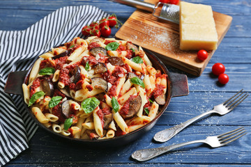Pan with tasty macaroni, napkin, kitchen board and forks on wooden table