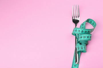 Measuring tape wrapped around fork lying on color surface. Diet concept