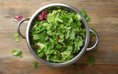 Colander with mixed salad leaves on wooden table