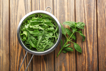 Arugula with basil in colander on wooden table