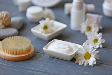 Fototapeta na wymiar Spa concept. Nourishing cream and daisy flowers on grey wooden table