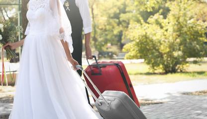 Bride and groom with big suitcases walking outdoors