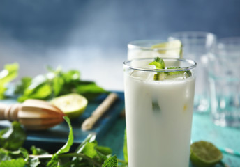 Obraz na płótnie Canvas Glass of tasty milk shake with lime and mint on table, closeup