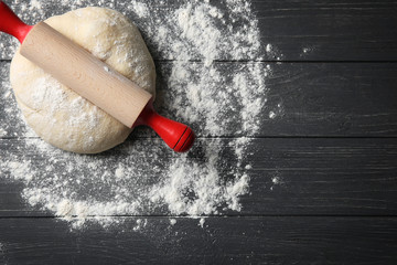 Dough for pizza and rolling pin with flour on wooden table