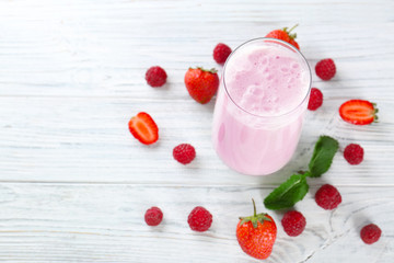 Glass of delicious milkshake and fresh berries on white wooden background