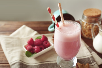 Glass of delicious berry milkshake and fresh raspberry on napkin