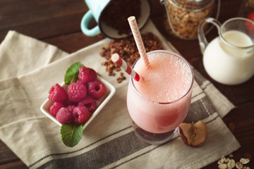 Glass of delicious berry milkshake and fresh raspberry on napkin