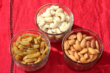 Dry fruits almond, cashew and raisin in glass bowls on red background