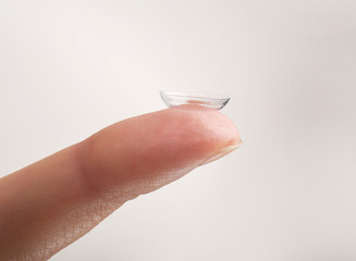 Contact lens on female finger against light background, close up view. Medicine and vision concept