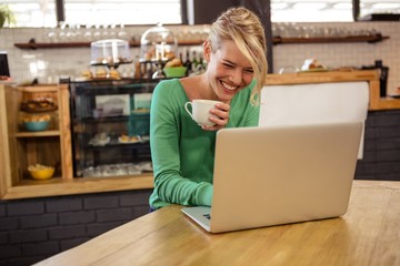 Woman drinking coffee and using laptop