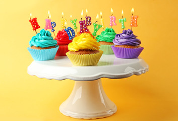 Tasty colorful cupcakes with Happy Birthday candles and plastic stand on yellow background