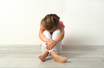 Sad little girl sitting on floor in empty room