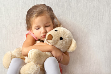 Sad little girl with teddy bear on light background