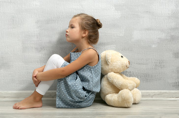 Offended little girl with teddy bear sitting on floor in empty room