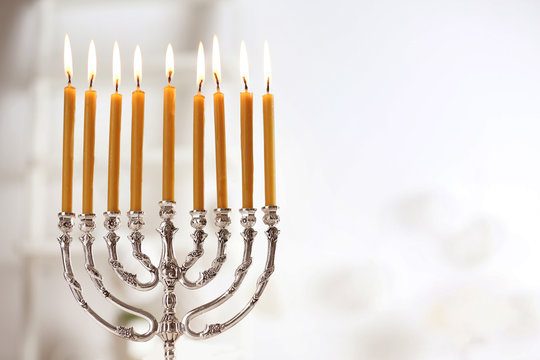 Beautiful menorah with burning candles on light blurred background. Hanukkah concept