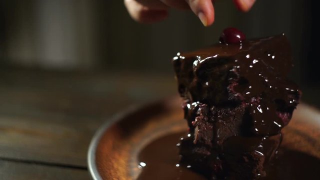 Chef put cherry to brownie chocolate cake. Homemade cake. Closeup of delicious dessert on kitchen. Chocolate topping on dessert. Chocolate brownie. Sweet food. Tasty dessert. Brownie cake