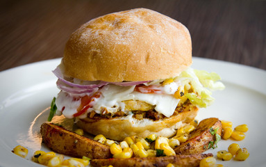 Side view of a healthy egg burger with mayo, corn, potato wedges and more
