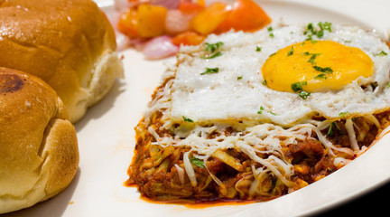 Close up shot of a fried egg on Indian thick gravy with buns and salad