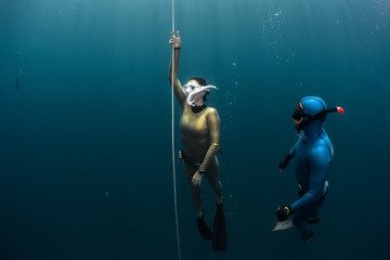 Two lady free diver ascending along the rope in the depth