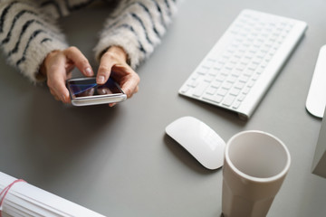frau sitzt am schreibtisch und tippt auf ihrem mobiltelefon