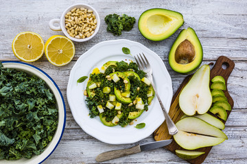Fresh salad with kale leaves and avocado with pear on a white plate on wooden table.

