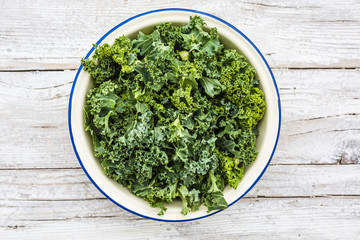 Fresh and raw kale leaves in a bowl on a wooden background.