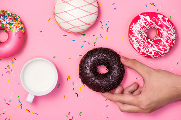 Donuts, sweetmeats candy on pink background. Hand holds donut.