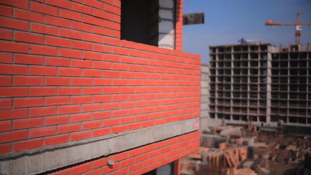 The construction of the condominium . The camera goes up along the wall of a brick house. In the background an unfinished house