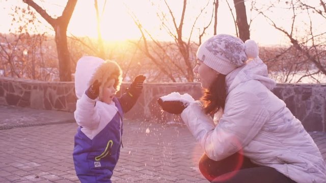 Beautiful happy young Family having fun outdoors at winter. Happy laughing mother with little baby boy playing in winter park with sun and sunshine. Mom and child play with snow. Slow motion, Slowmo