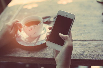 Close-up Of Woman Holding Mobile Phone In Front Of Coffee Cup