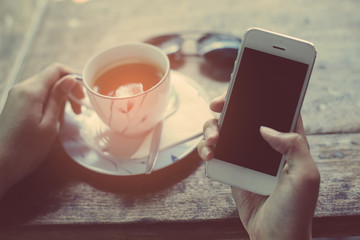 Close-up Of Woman Holding Mobile Phone In Front Of Coffee Cup