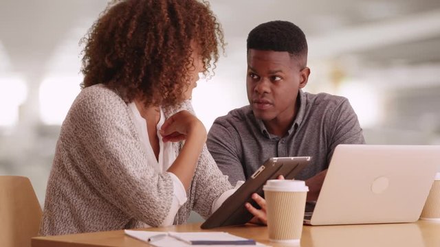 Millennial coworkers comparing notes using tablets and laptops
